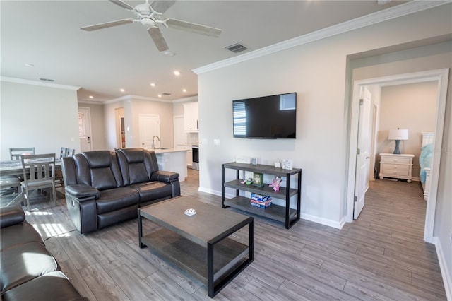 living room with light wood-type flooring, ceiling fan, ornamental molding, and sink