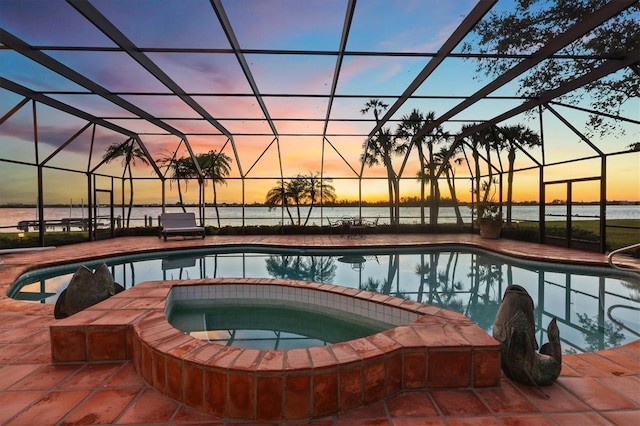 pool at dusk featuring an in ground hot tub, a water view, and a lanai