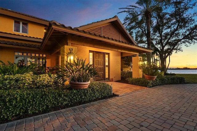 exterior space featuring a tiled roof, a water view, and stucco siding