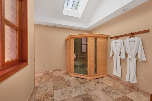 bathroom with lofted ceiling with skylight, stone finish floor, and baseboards