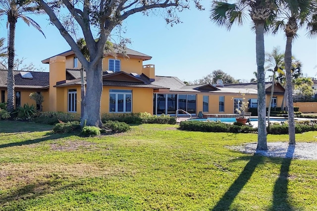 rear view of house featuring stucco siding, an outdoor pool, and a yard