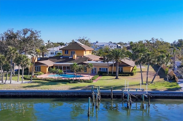 rear view of property featuring a lawn, an outdoor pool, and a water view