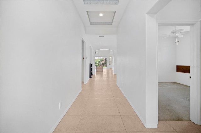 hall with a raised ceiling and light tile patterned flooring