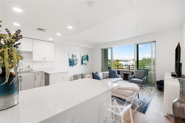 kitchen with white cabinets, a kitchen bar, dishwasher, and light wood-type flooring