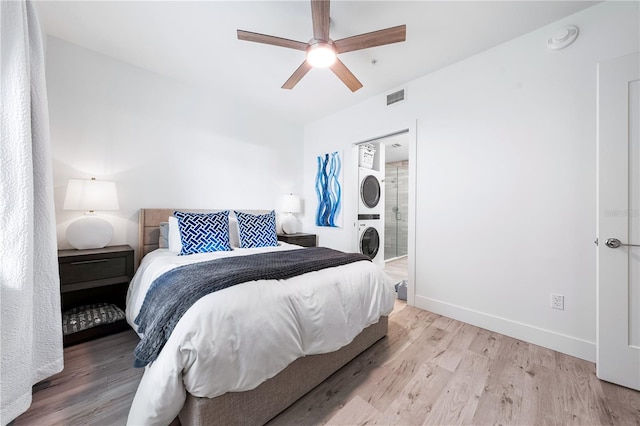 bedroom featuring ensuite bath, stacked washer / dryer, ceiling fan, and light wood-type flooring