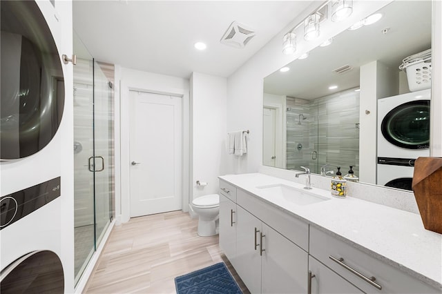 bathroom featuring toilet, stacked washing maching and dryer, a shower with shower door, and vanity