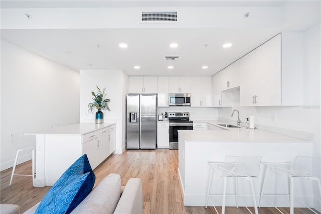 kitchen with stainless steel appliances, white cabinetry, a breakfast bar, and light wood-type flooring