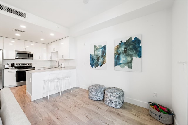 kitchen with kitchen peninsula, stainless steel appliances, light hardwood / wood-style flooring, and white cabinetry