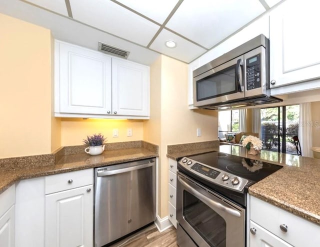 kitchen with dark stone countertops, appliances with stainless steel finishes, light hardwood / wood-style flooring, and white cabinets