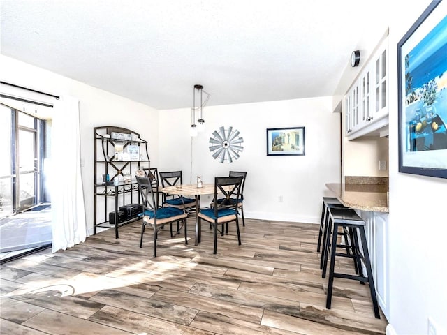 dining area featuring a textured ceiling, wood finished floors, and baseboards
