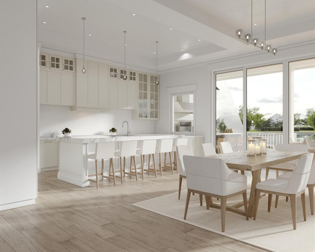 dining space featuring light wood-type flooring, a raised ceiling, a wealth of natural light, and sink