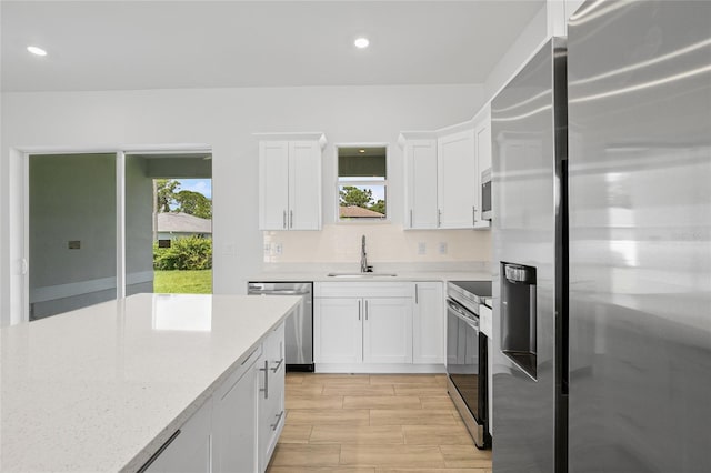 kitchen with light hardwood / wood-style floors, sink, white cabinets, stainless steel appliances, and light stone countertops