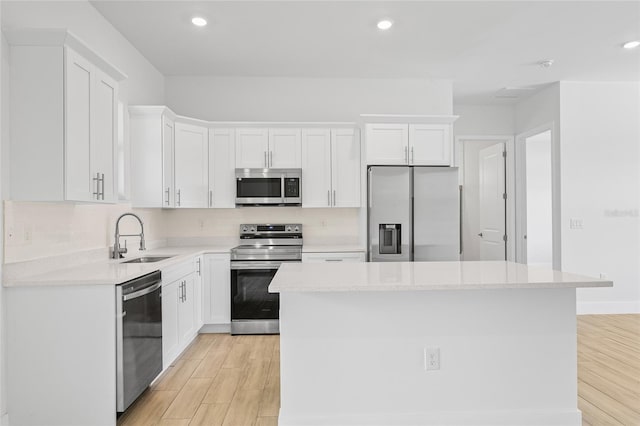 kitchen with light hardwood / wood-style floors, white cabinetry, stainless steel appliances, a center island, and sink