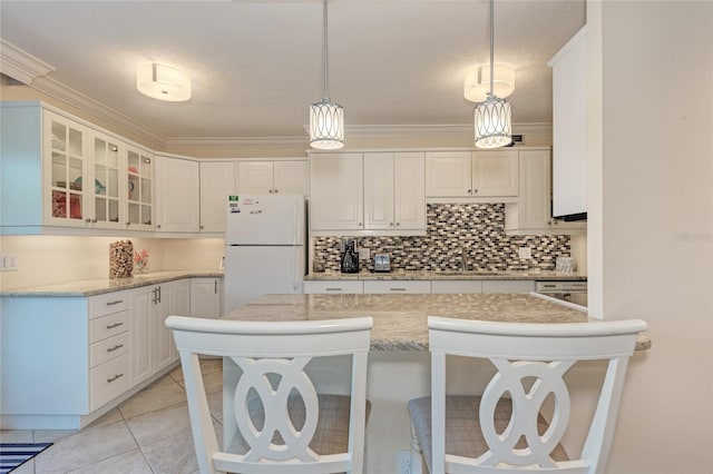 kitchen featuring a breakfast bar, freestanding refrigerator, tasteful backsplash, glass insert cabinets, and crown molding