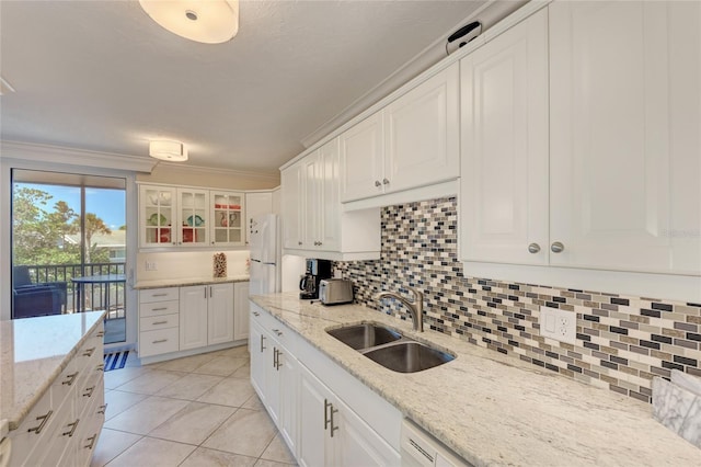 kitchen with tasteful backsplash, glass insert cabinets, freestanding refrigerator, crown molding, and a sink