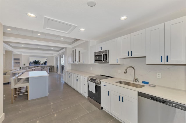 kitchen featuring stainless steel appliances, a raised ceiling, open floor plan, white cabinets, and a sink