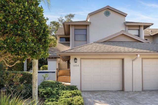 view of front of house featuring decorative driveway, roof with shingles, an attached garage, and stucco siding