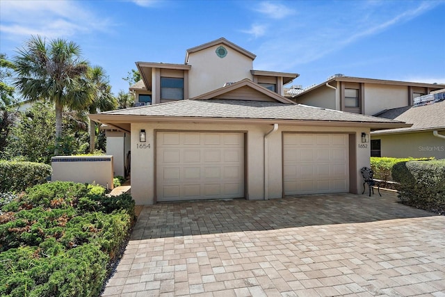 view of front of home with a garage, decorative driveway, roof with shingles, and stucco siding