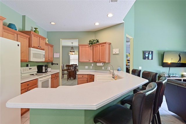 kitchen featuring light tile patterned flooring, a kitchen bar, white appliances, and kitchen peninsula