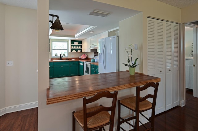 kitchen featuring white appliances, visible vents, dark wood finished floors, a sink, and green cabinets