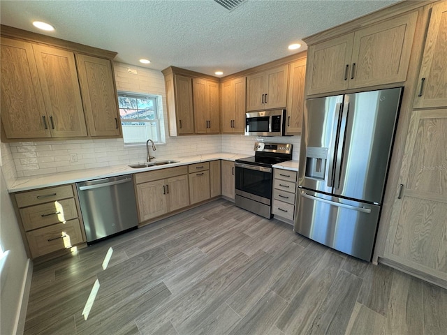 kitchen with hardwood / wood-style floors, appliances with stainless steel finishes, sink, a textured ceiling, and tasteful backsplash