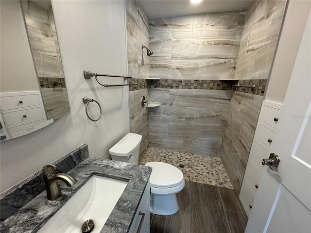 bathroom with vanity, toilet, hardwood / wood-style flooring, and tiled shower