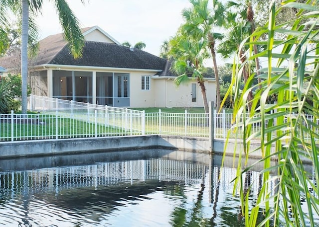 rear view of house with a sunroom, a water view, and a yard