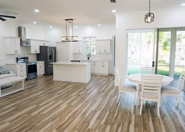 kitchen featuring appliances with stainless steel finishes, wall chimney exhaust hood, white cabinets, and pendant lighting