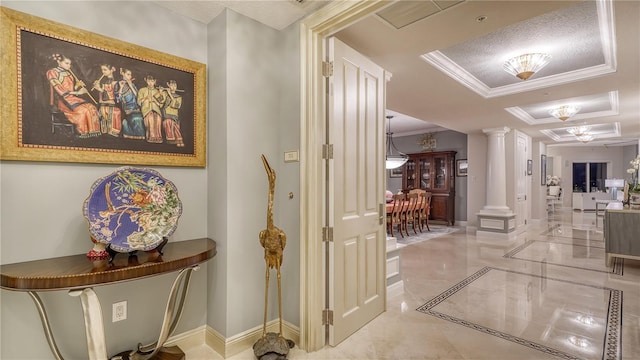 hallway with decorative columns, a textured ceiling, a raised ceiling, and ornamental molding