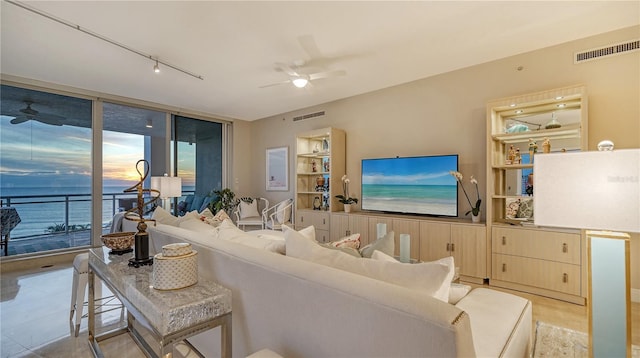 living room featuring ceiling fan, track lighting, floor to ceiling windows, and a water view