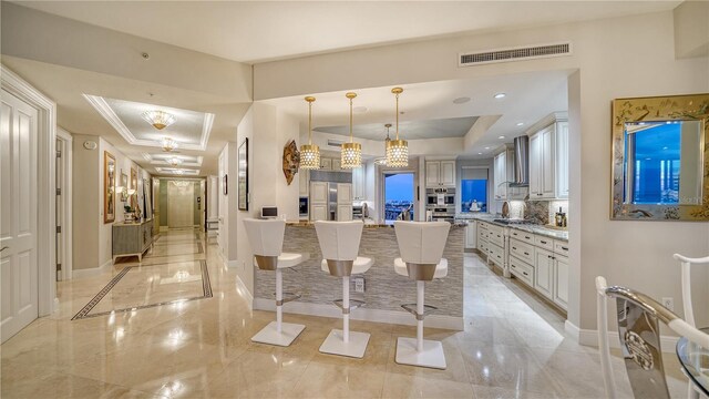 kitchen featuring hanging light fixtures, a kitchen island with sink, a raised ceiling, paneled fridge, and a breakfast bar area