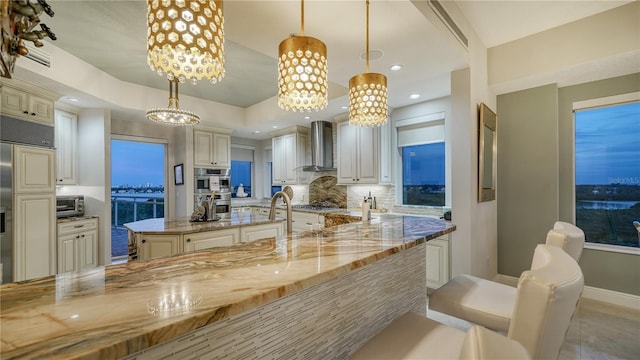 kitchen featuring pendant lighting, light stone counters, wall chimney range hood, and decorative backsplash