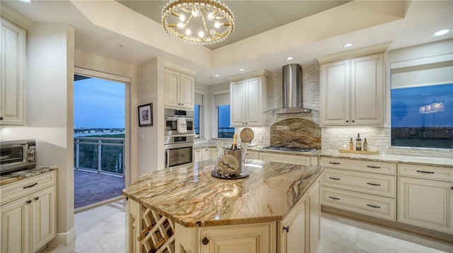 kitchen featuring light stone countertops, wall chimney exhaust hood, a kitchen island, decorative light fixtures, and stainless steel appliances