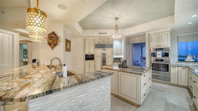 kitchen featuring light stone countertops, hanging light fixtures, a raised ceiling, and a large island