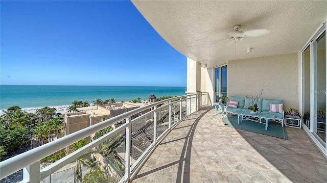 balcony featuring a beach view, ceiling fan, and a water view