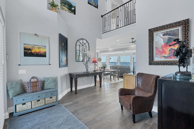 living area with hardwood / wood-style flooring, ceiling fan, and a high ceiling