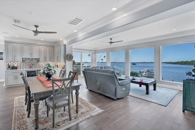 dining space with crown molding, light wood-type flooring, beverage cooler, and a water view