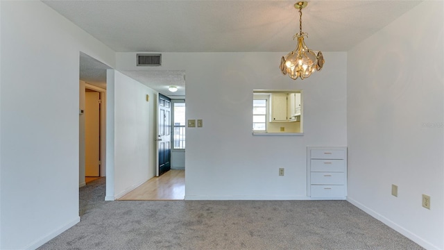 carpeted empty room with a chandelier and a textured ceiling