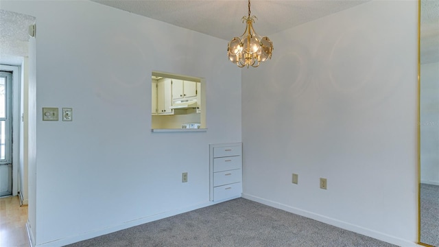 unfurnished room featuring light carpet, a textured ceiling, and an inviting chandelier