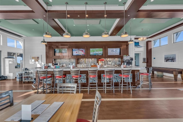 kitchen with dark hardwood / wood-style flooring, decorative backsplash, hanging light fixtures, a breakfast bar, and coffered ceiling