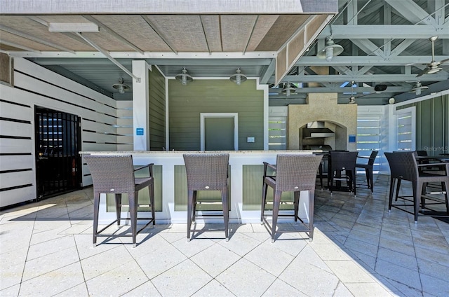 view of patio with a bar, an outdoor fireplace, and ceiling fan