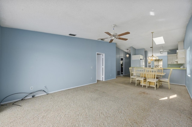 unfurnished dining area with a textured ceiling, light colored carpet, ceiling fan, and vaulted ceiling with skylight