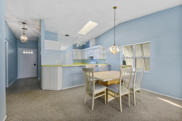 dining space featuring ceiling fan with notable chandelier, light colored carpet, and lofted ceiling with skylight