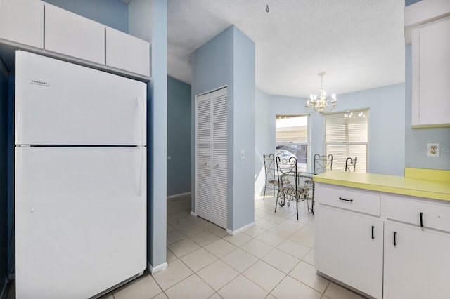 kitchen with a textured ceiling, a notable chandelier, white fridge, white cabinetry, and hanging light fixtures