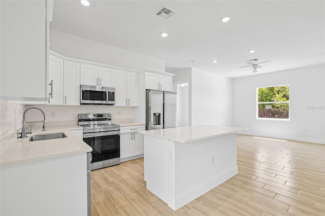 kitchen with appliances with stainless steel finishes, tasteful backsplash, sink, white cabinets, and a center island