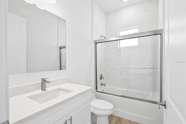 full bathroom featuring bath / shower combo with glass door, hardwood / wood-style floors, vanity, and toilet