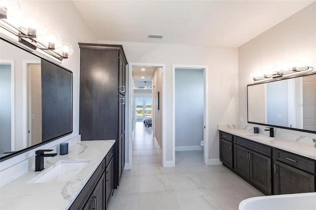 bathroom featuring baseboards, visible vents, toilet, a sink, and two vanities