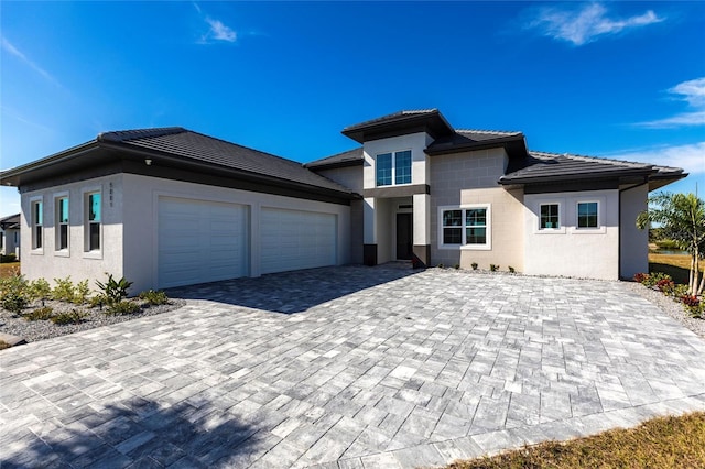 prairie-style house with a garage, decorative driveway, a tiled roof, and stucco siding