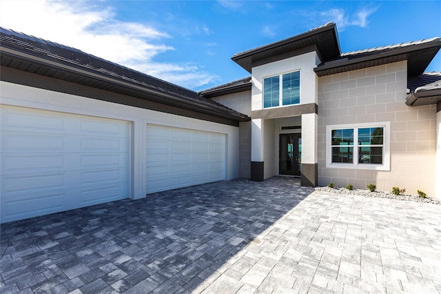 view of front of home with decorative driveway, concrete block siding, an attached garage, and stucco siding