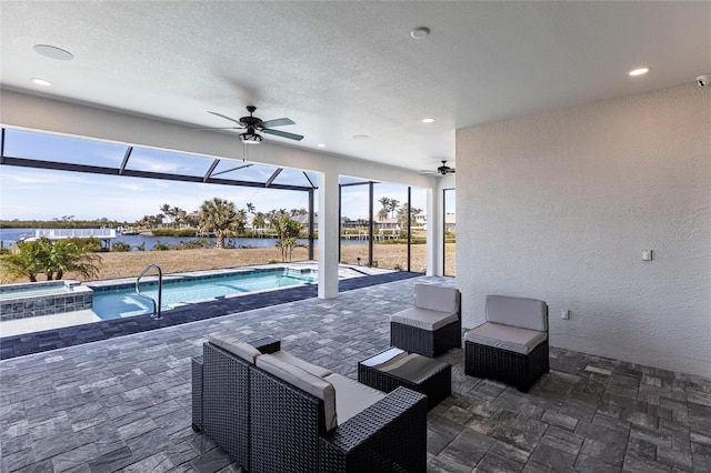 view of swimming pool featuring glass enclosure, a water view, a pool with connected hot tub, a ceiling fan, and a patio area